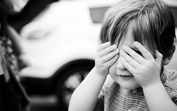black and white reportage wedding photography of young guest hiding behind his fingers